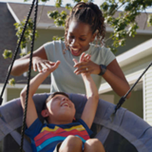 An adoptive mom pushes a boy on a swing.
